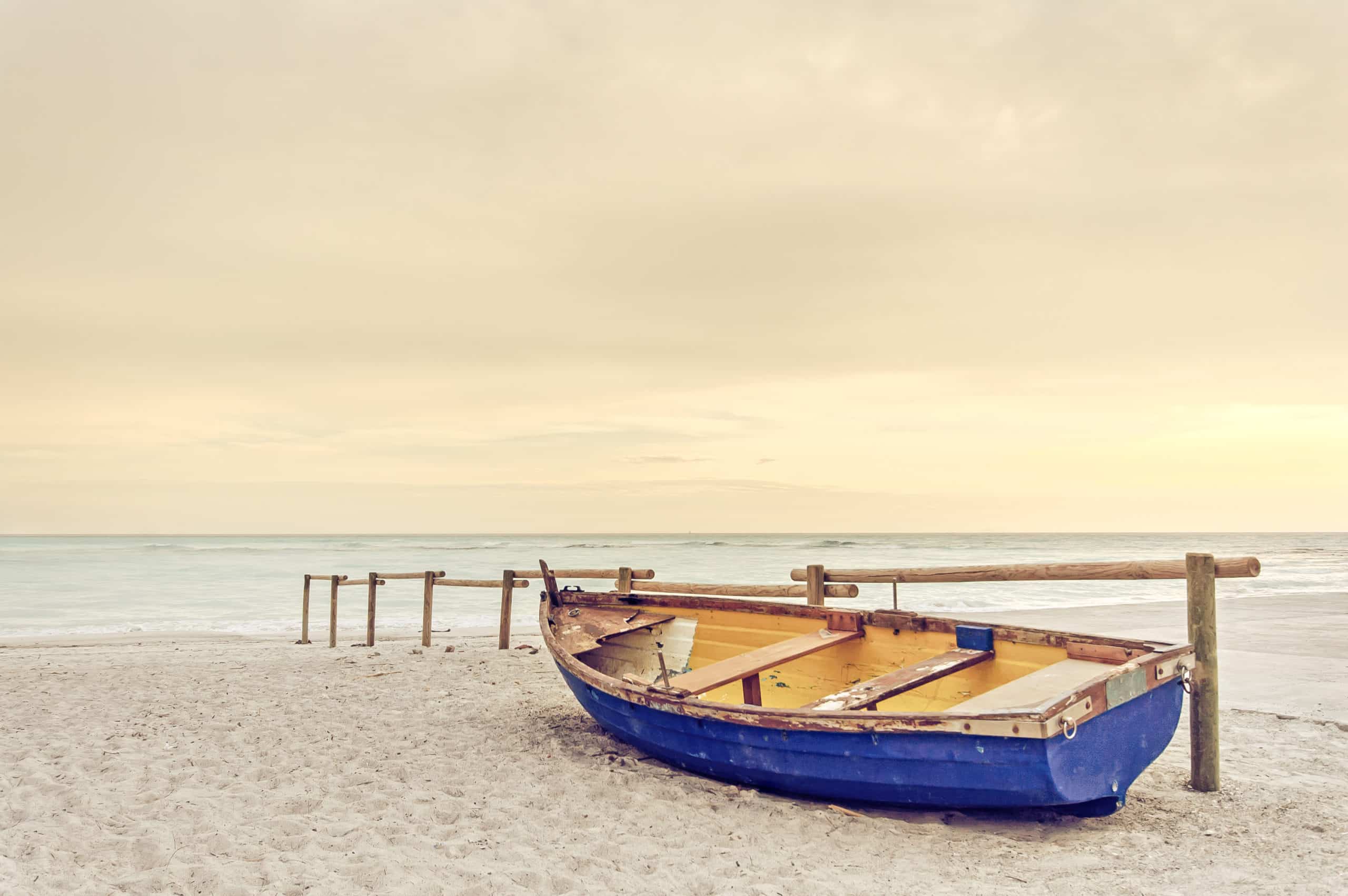 Old yellow blue wooden boat on white beach. warm sunset